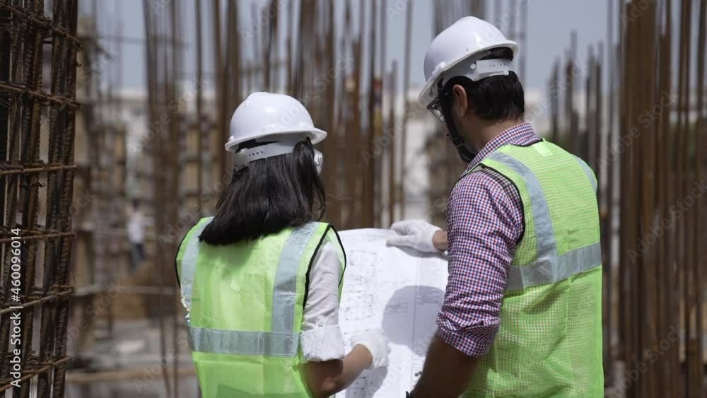 Two Indian engineers lady and man wearing safety helmets and face mask with eyeglass they have a discussing conversation together on construction site.Foreman and his assistant lady talking together. Two Indian engineers lady and man wearing safety helmets and face mask with eyeglass they have a discussing conversation together on construction site.Foreman and his assistant lady talking together.