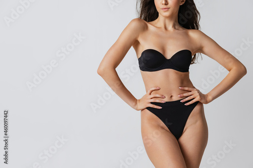 Cropped image of sportive female body in black lingerie posing isolated on light gray studio background. Natural beauty concept.