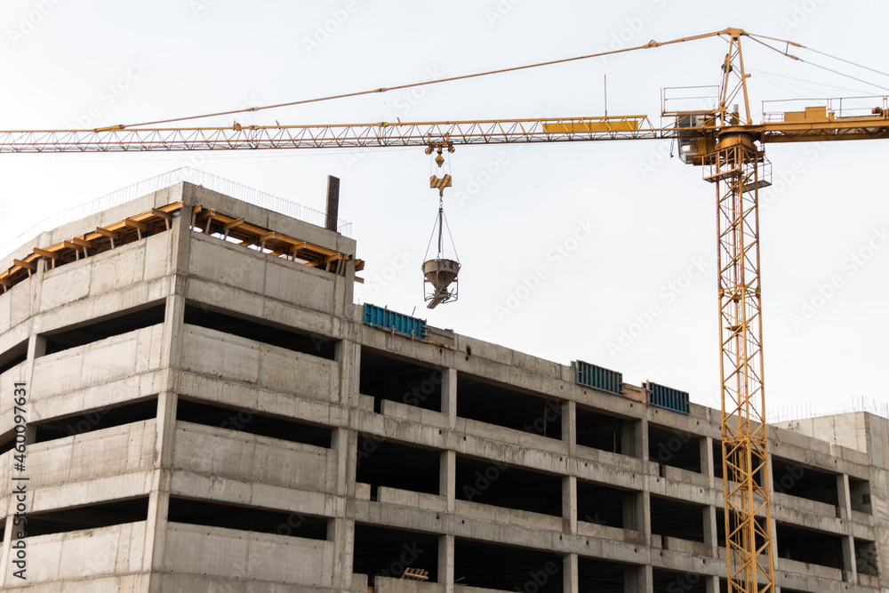 A construction tower crane lifts a concrete mixer to the roof of a building under construction. Crane work at a construction site. A construction tower crane lifts a concrete mixer to the roof of a building under construction. Crane work at a construction site.