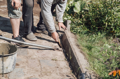 Men lay curbstone for grouting garden path, construction work on garden plot