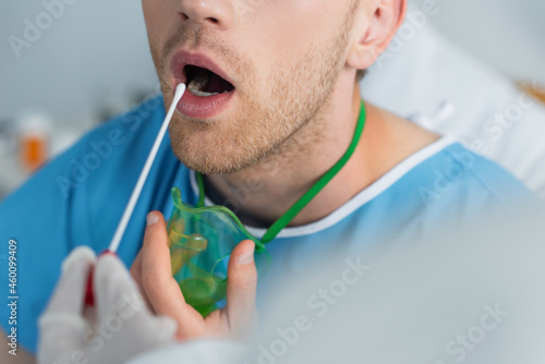 cropped view of doctor holding swab near patient with open mouth