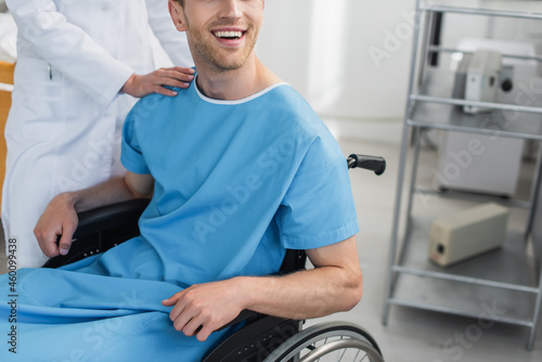 cropped view of doctor in white coat standing near cheerful disabled patient in wheelchair