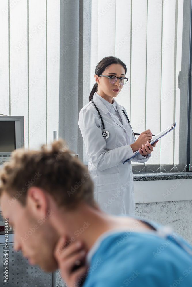 Fototapeta premium brunette doctor looking at blurred patient suffering from sore throat in hospital