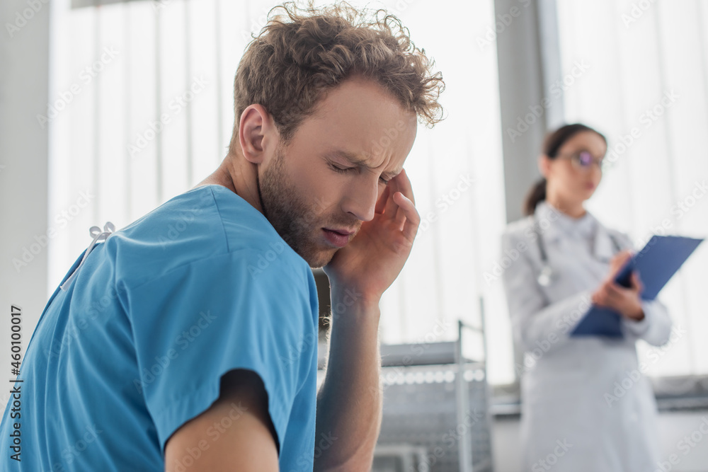 curly patient suffering from headache near blurred doctor in hospital curly patient suffering from headache near blurred doctor in hospital