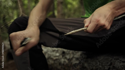 Hunter man with knife cut a wooden stick. Survivalist