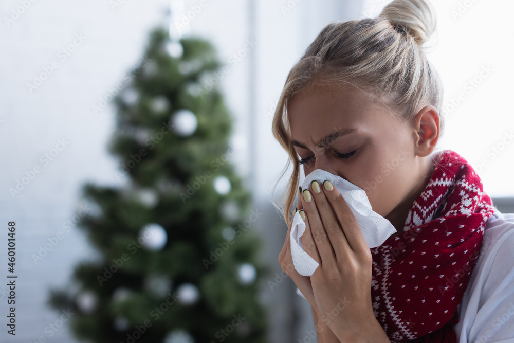 sick woman sneezing in paper napkin near christmas tree on blurred  background Stock Photo | Adobe Stock
