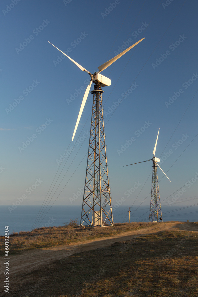 Wind generators on the mountain hill at sunset. Renewable energy source. Wind power plant. Cape Meganom, Crimea. Wind generators on the mountain hill at sunset. Renewable energy source. Wind power plant. Cape Meganom, Crimea.
