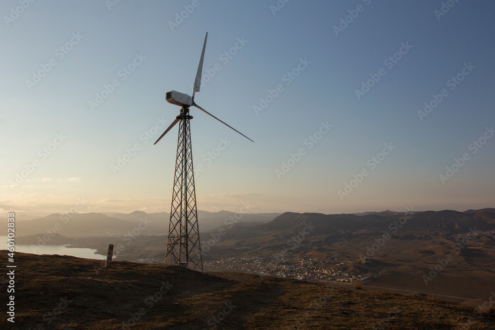 Single wind turbine on the mountain hill at sunset. Renewable source of energy. Green energy generation. Cape Meganom, Crimea. Single wind turbine on the mountain hill at sunset. Renewable source of energy. Green energy generation. Cape Meganom, Crimea.