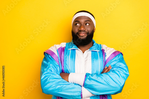 Photo of thoughtful cute dark skin man wear blue suit headband hands folded looking empty space smiling isolated yellow color background