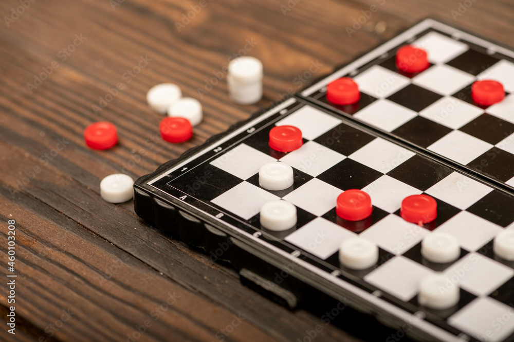 A board for playing checkers with chips on a wooden table, close-up, selective focus. A board for playing checkers with chips on a wooden table, close-up, selective focus.