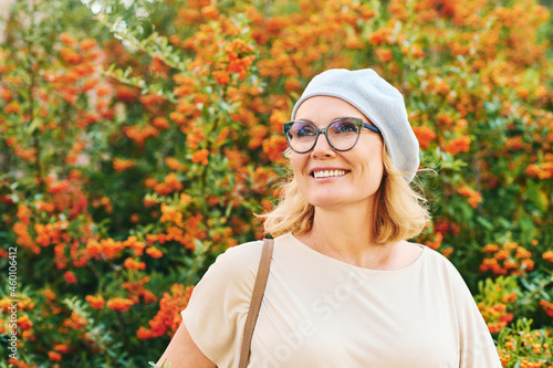 Outdoor portrait of happy middle age woman posing next to bright orange scarlet firethorn berries (Pyracantha coccinea) photo