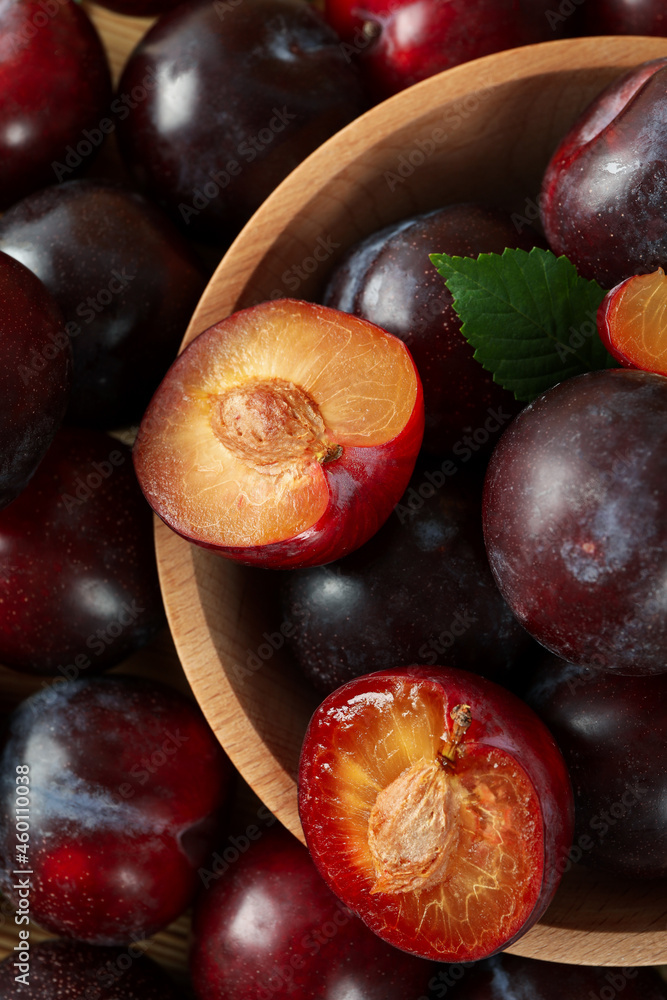 Fototapeta premium Wooden bowl with plums on plums background
