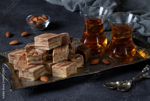 Tea ceremony with Uzbek sweet milk halva with almonds and cocoa on dark background.