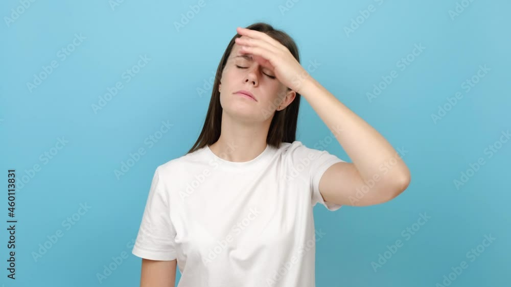Portrait of unhappy sad young brunette woman suffering from headache, frustrated dizzy flu-sick girl feeling unwell, fever and flue symptoms, stress tension, isolated on blue studio background wall Portrait of unhappy sad young brunette woman suffering from headache, frustrated dizzy flu-sick girl feeling unwell, fever and flue symptoms, stress tension, isolated on blue studio background wall