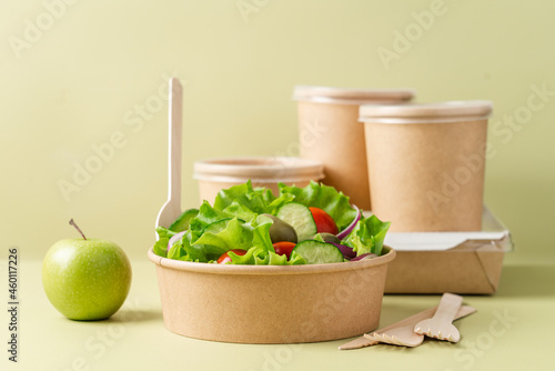 Healthy vegetable salad in recyclable cardboard container. Food delivery, healthy food menu for home or office concept. Green background, side view