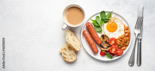Traditional English breakfast with fried egg, beans in tomato sauce, grilled sausages, mushrooms and fresh tomatoes, served on plate. White background^ flat lay