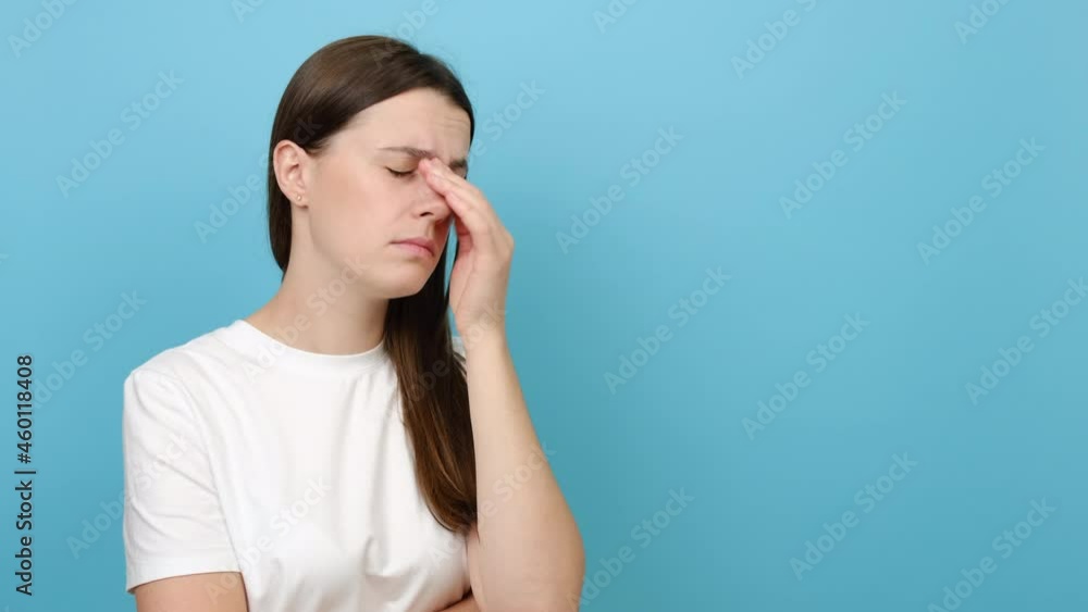 Tired young brunette female 20s old years massaging nose bridge, feeling eye strain, exhausted lady suffering from headache or migraine, posing isolated on blue studio background. Eyes fatigue concept Tired young brunette female 20s old years massaging nose bridge, feeling eye strain, exhausted lady suffering from headache or migraine, posing isolated on blue studio background. Eyes fatigue concept