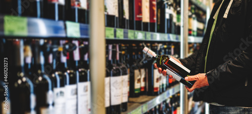 man hand holding bottle wine in grocery store in supermarket