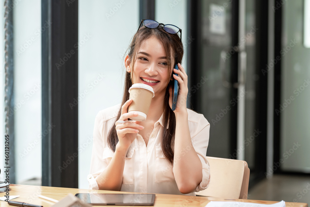 Beautiful young Asian businesswoman happy and successful sitting talking on the mobile phone and holding coffee at the office . Beautiful young Asian businesswoman happy and successful sitting talking on the mobile phone and holding coffee at the office .
