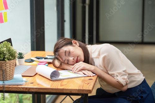 Overwork of young Asian businesswoman makes her tired and asleep at the office desk with paperwork.