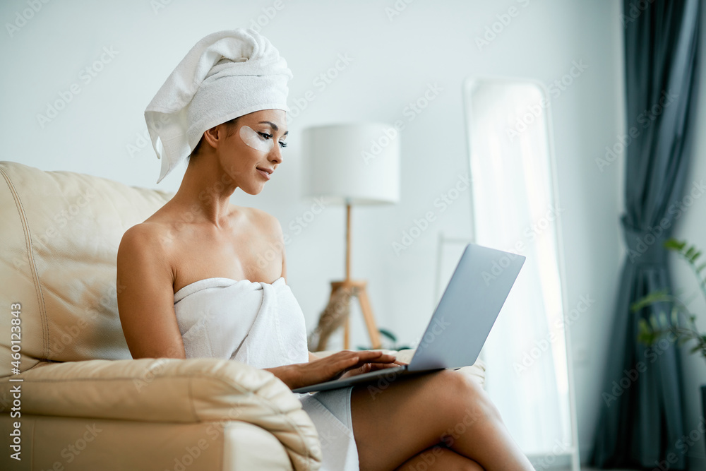 Young woman surfing the net on laptop while using under eye recovery patch at home. Young woman surfing the net on laptop while using under eye recovery patch at home.