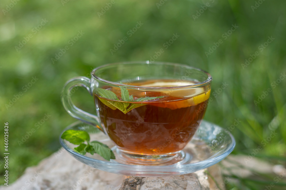 Tea in bloom stands on a stone in the garden, served with lemon and fresh mint leaves. .Selective Focus glass Tea in bloom stands on a stone in the garden, served with lemon and fresh mint leaves. .Selective Focus glass