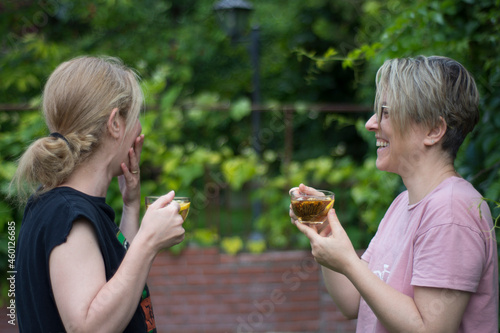 two young sister women are drinking blooming tea and chatting in the garden of their house. Selective Focus Glasses