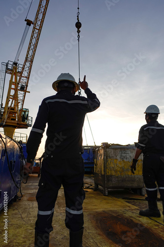 Rigger standing raising using a hand signal by moving finger slowly to directing communication with crane driver to move the boom up at offshore oil and gas platform