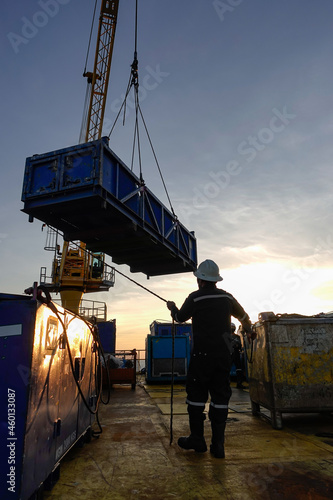 Rigger hold rope for conrol cargo while crane driver move the boom up at offshore oil platform