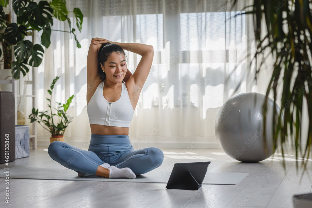 Young Asian woman exercising at home, attending an online yoga class, stretching. Daily sports routines for a healthy lifestyle and stress relief.