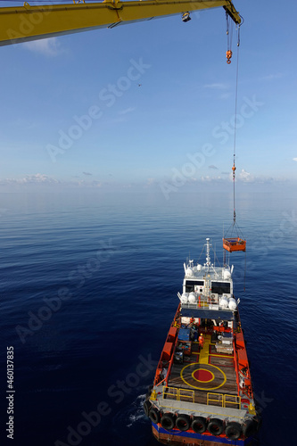 Cargo being loaded from a oil and gas platform onto a supply vessel and vessel crew give hand signal for lifting.
