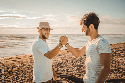 Portrait of two smiling guys on the beach shaking hands - Happy best friends greeting each other with a handshake