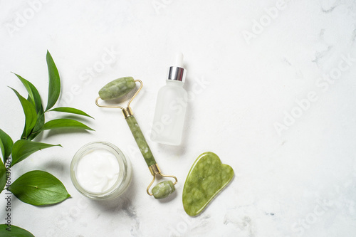 Face massage set on white. Jade roller and gua sha stone massager with face cream and serum bottle. Top view.