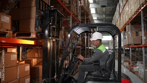 Close-up of warehouse worker operating forklift, placing pallet full of cardboard boxes on shelf. Professional forklift driver lifting goods on rack filled with cardboard boxes