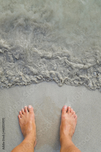 Putting man feet inside the water wave on a sandy beach