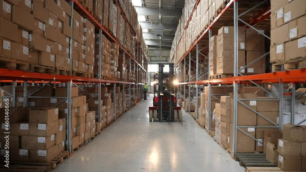 Warehouse machinery at work, forklift driver riding between rows of ...