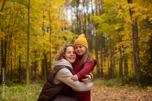 smilling mother with curly hair and a little daughter walk in the autumn park