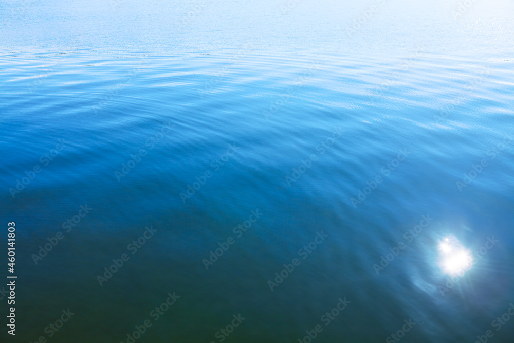 Blue water surface with sun glowing reflection