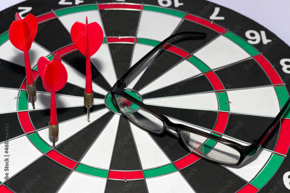 Poor vision concept, darts game, miss on target with darts and glasses Poor vision concept, darts game, miss on target with darts and glasses