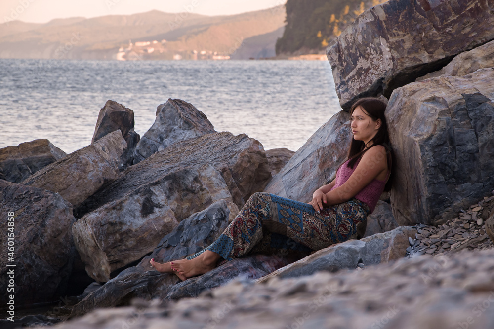a girl sits on a stone shore and looks at the horizon a girl sits on a stone shore and looks at the horizon