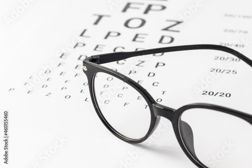Eyeglasses with black frame on visual test chart isolated on white. Eyesight, healthcare and medicine concept.