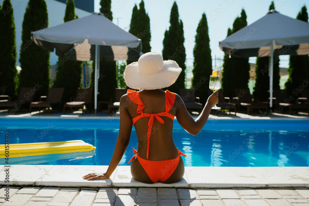 Sexy woman sitting at the edge of pool, back view