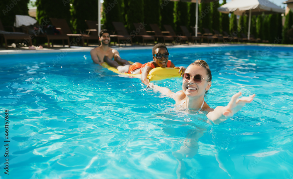 Cheerful friends swim on a mattress in the pool