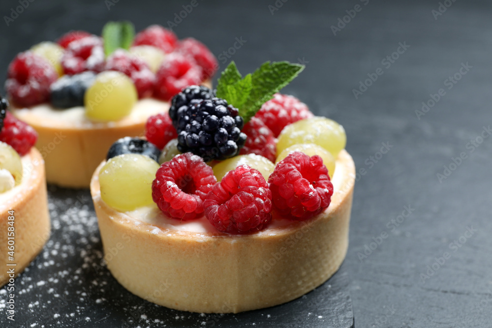 Delicious tartlets with berries on black table, closeup