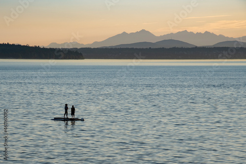 People in silhouette out on floating dock raft looking at mountain peaks at sunset.