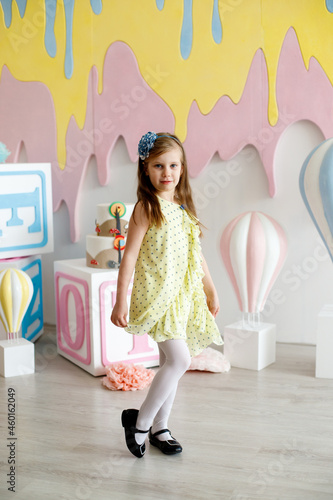 A girl in a yellow dress with black polka dots poses in a photo studio.