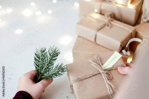 Spruce twigs in a child's hand and a handmade gift in kraft paper with the inscription Merry Christmas on a white table. Plastic free sustainable lifestyle