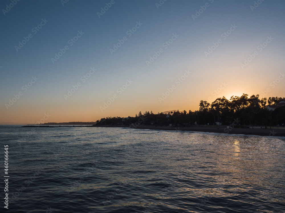 Naklejka premium Beautiful sunset by the Mediterranean sea with the silhouette of trees and palm trees in the background