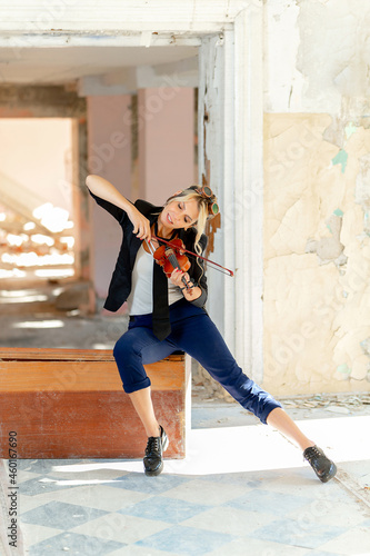 A beautiful young woman plays the violin in an old abandoned house on the ruins of the city.