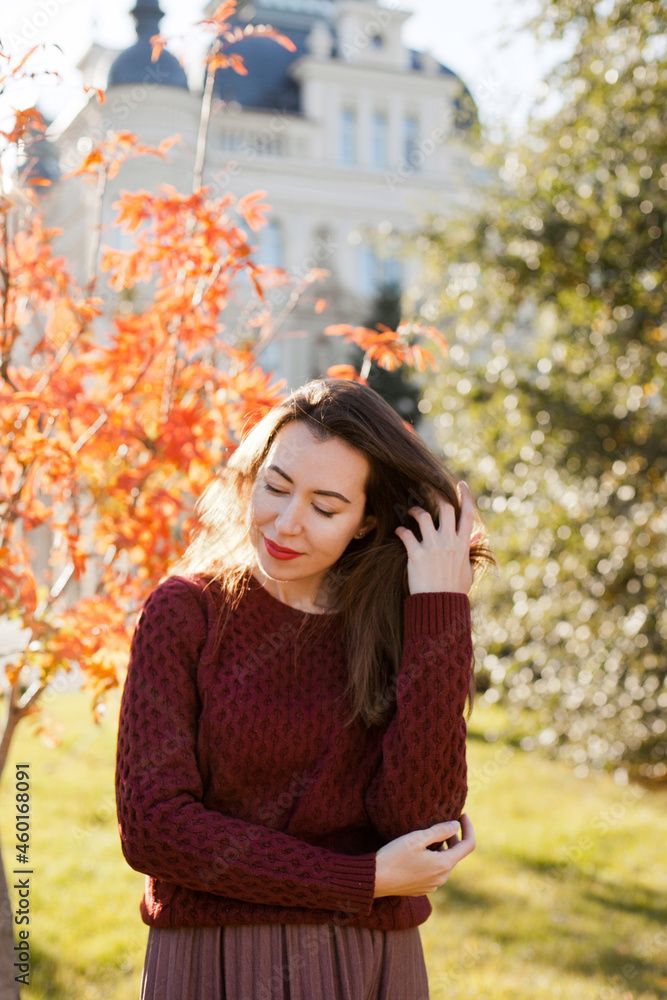 Beautiful woman in burgundy sweater walking in autumn park, fixing hair Beautiful woman in burgundy sweater walking in autumn park, fixing hair